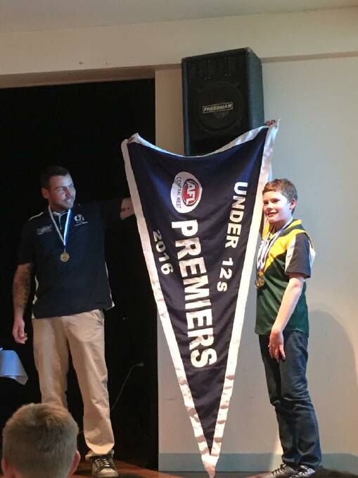 Under 12s Blues coach Marc Hyland and captain Djakai Reid unveil the premiership flag.